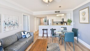 A modern living room with a grey sofa, a dining area with blue chairs, a kitchen with white cabinets, and a ceiling fan. - Newly renovated Ocean Front Deluxe King Condo,Come Live in the Paradise (Myrtle Beach)