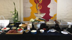 A buffet setup with various food items and a painting of two faces in the background. - Hotel Simple Plus (Vilnius)