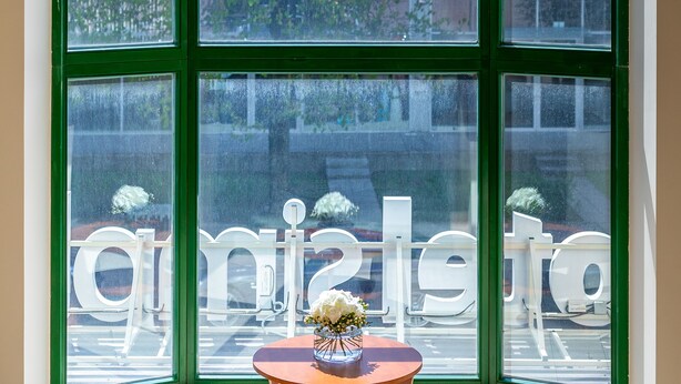 A corner room with a large window, a chandelier, and a small table with a vase. - Hotel Simple Plus (Vilnius)