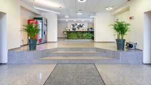 A hotel lobby with a Coca-Cola vending machine, two potted plants, a reception desk, and a "Hotel simple" sign on the floor. - Hotel Simple Plus (Vilnius)