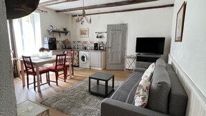 Un salon spacieux avec un canapé gris, un plancher en bois, un coin repas avec des chaises rouges, une cuisine équipée d’un lave-linge et un téléviseur.
