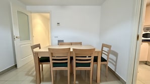 A dining area with a rectangular table and four chairs, each with a green cushion. - MESTRAL PB3 (L'Escala)
