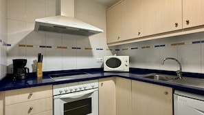 A kitchen with a white stove, a microwave, a sink, and cabinets. - MESTRAL PB3 (L'Escala)