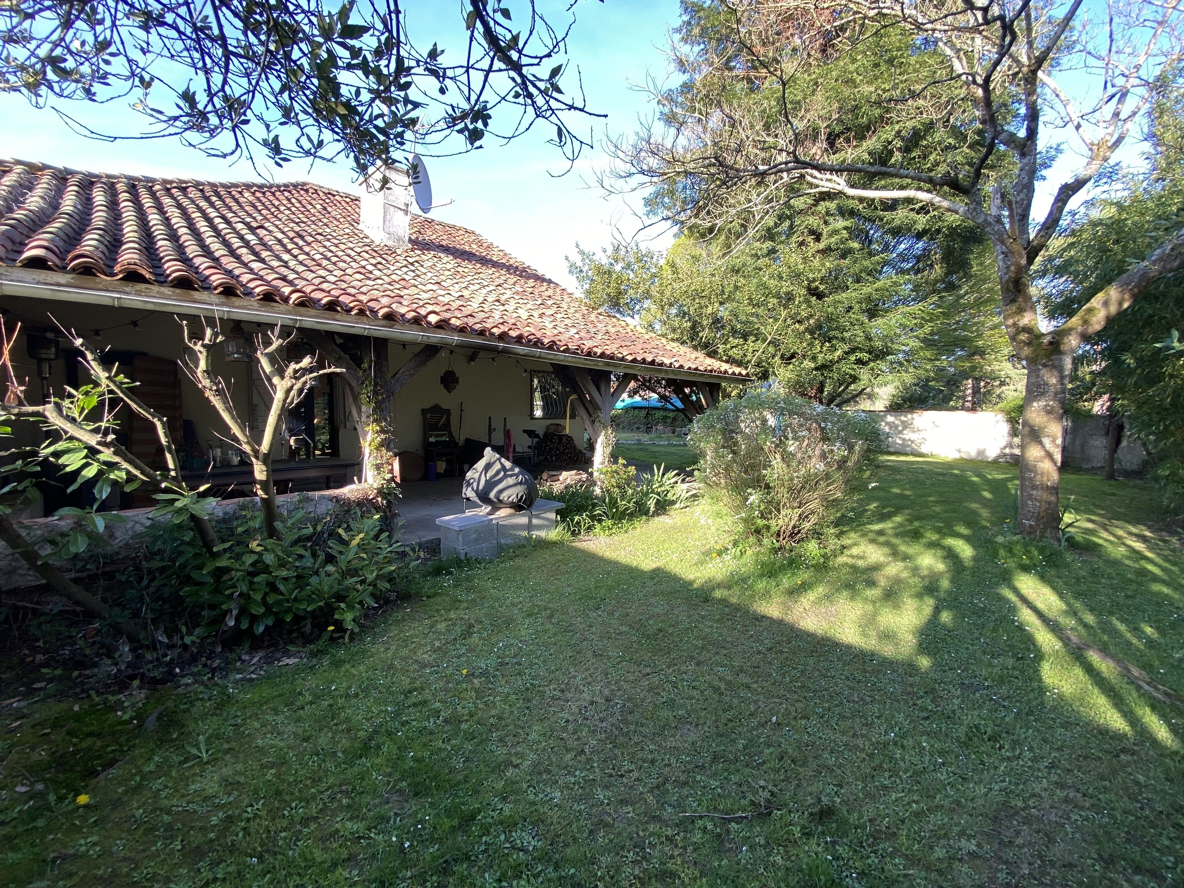 A house with a tiled roof, a porch, and a garden with grass and trees.