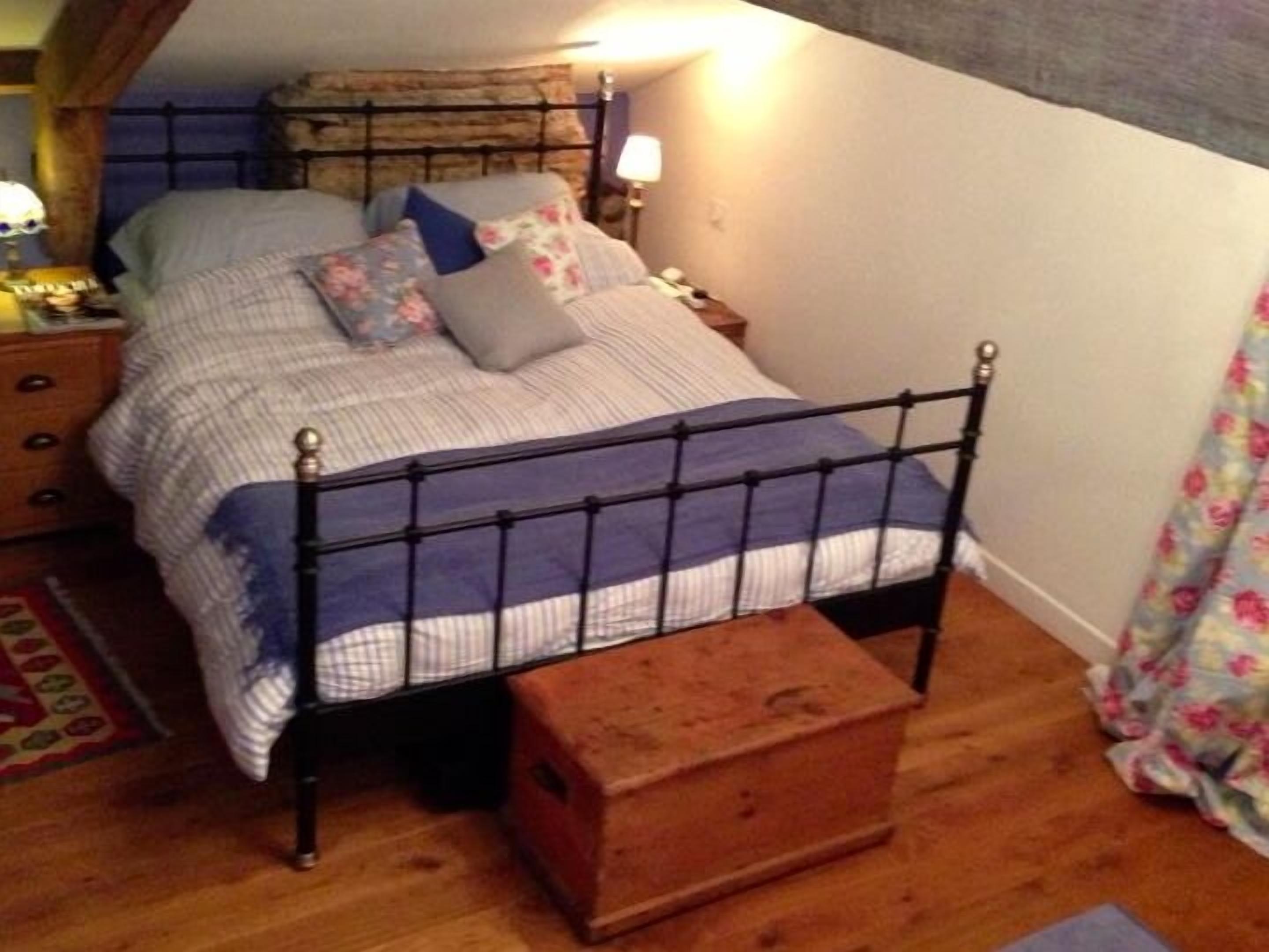 A bed with a metal frame, a wooden chest, and a nightstand with a lamp.