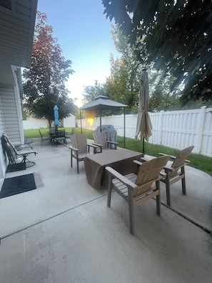 An outdoor patio with a table and chairs, a grill, and a covered seating area.