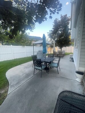 A patio with a table and chairs, a covered grill, and a white fence in the background. - ***Utah’s Utopia*** (West Jordan)