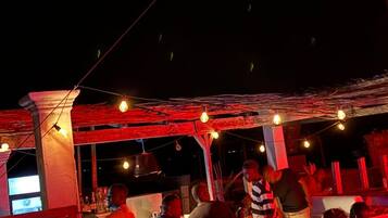 Un área de estar al aire libre con mesas y sillas, una zona de bar y una sección cubierta con luces colgantes.