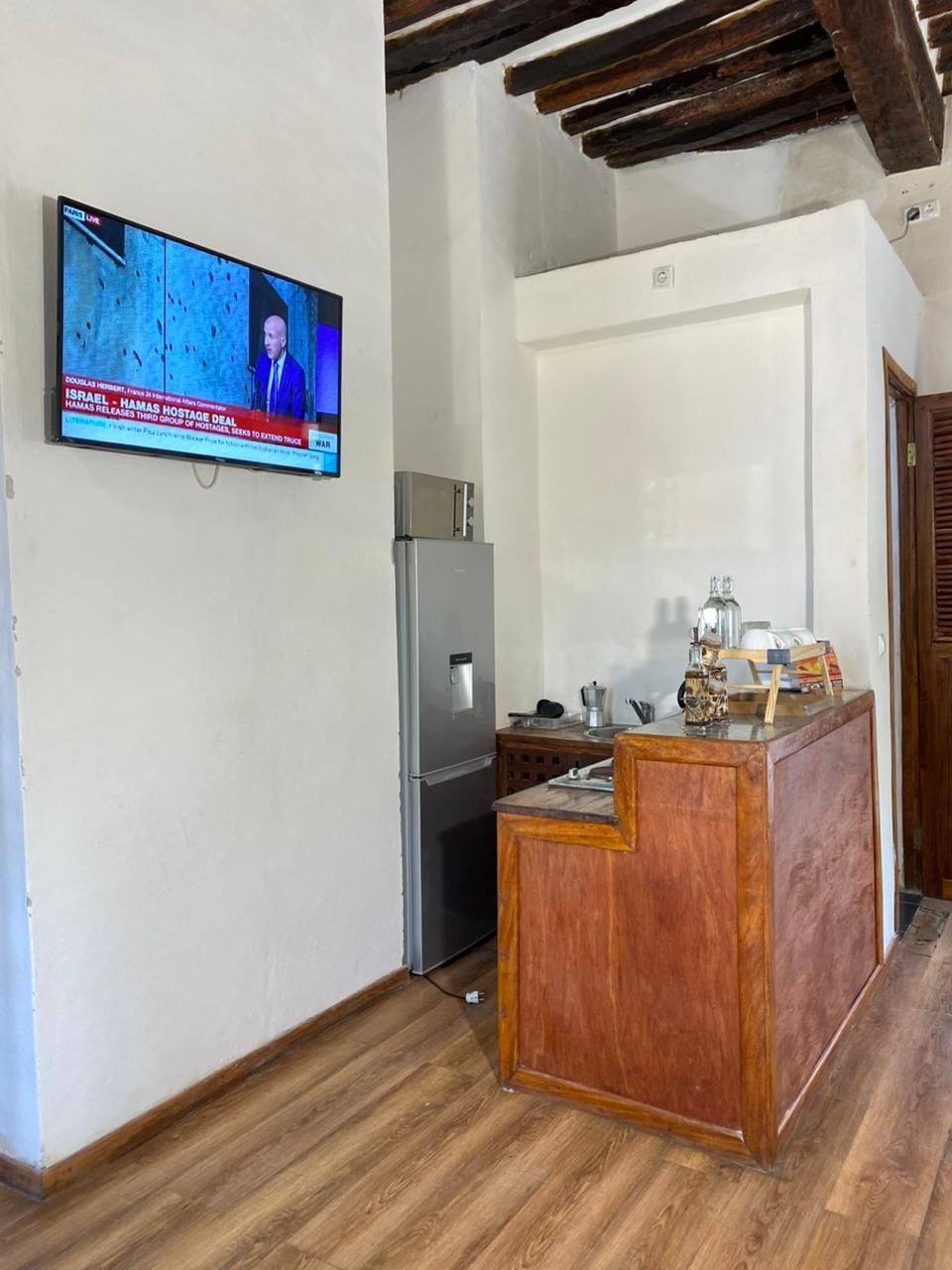 A kitchen with a wooden counter, a refrigerator, and a television displaying a news broadcast.