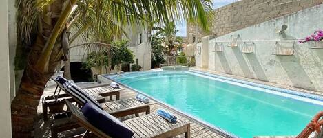 Un área de piscina con sillas de descanso, una hamaca y una palmera.