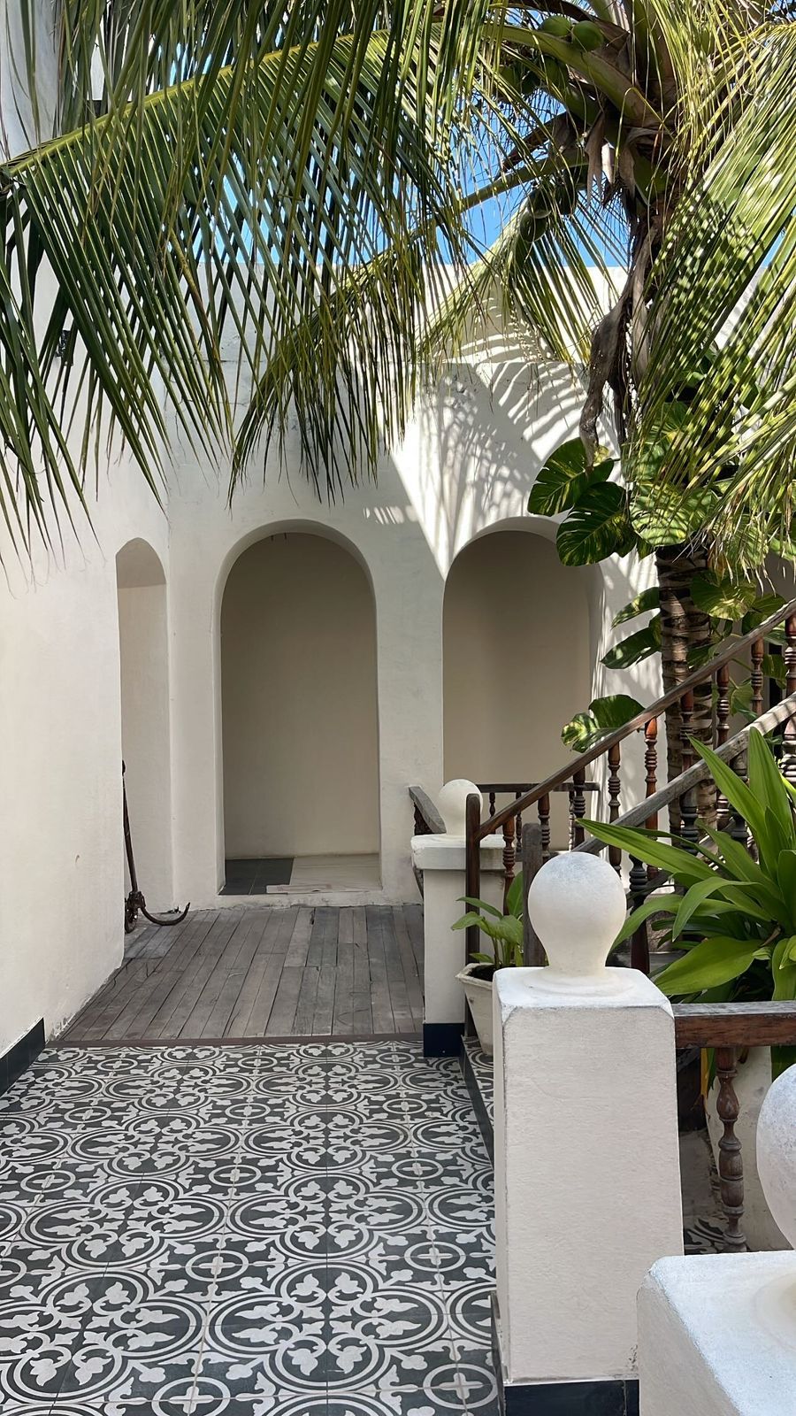 A courtyard with a patterned floor, a wooden staircase, and a white wall with arches.