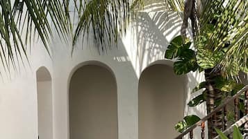 A courtyard with a patterned floor, a wooden staircase, and a white wall with arches.