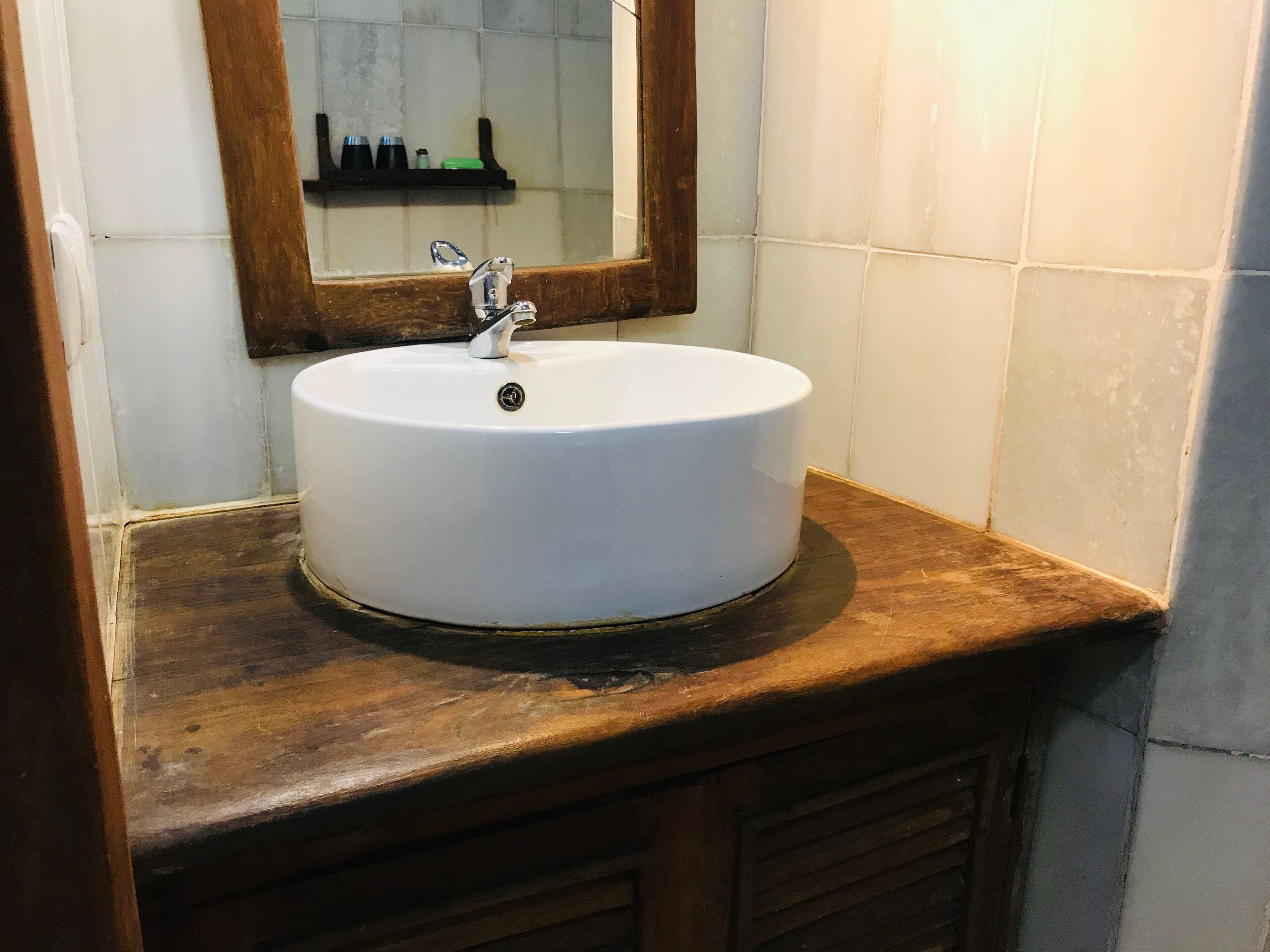 Une salle de bain avec un lavabo blanc, un plan de toilette en bois et un miroir au-dessus.