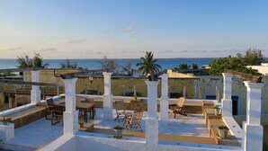 A rooftop terrace with outdoor seating, a view of the sea, and traditional architecture. - Cafe Central (Mozambique Island)