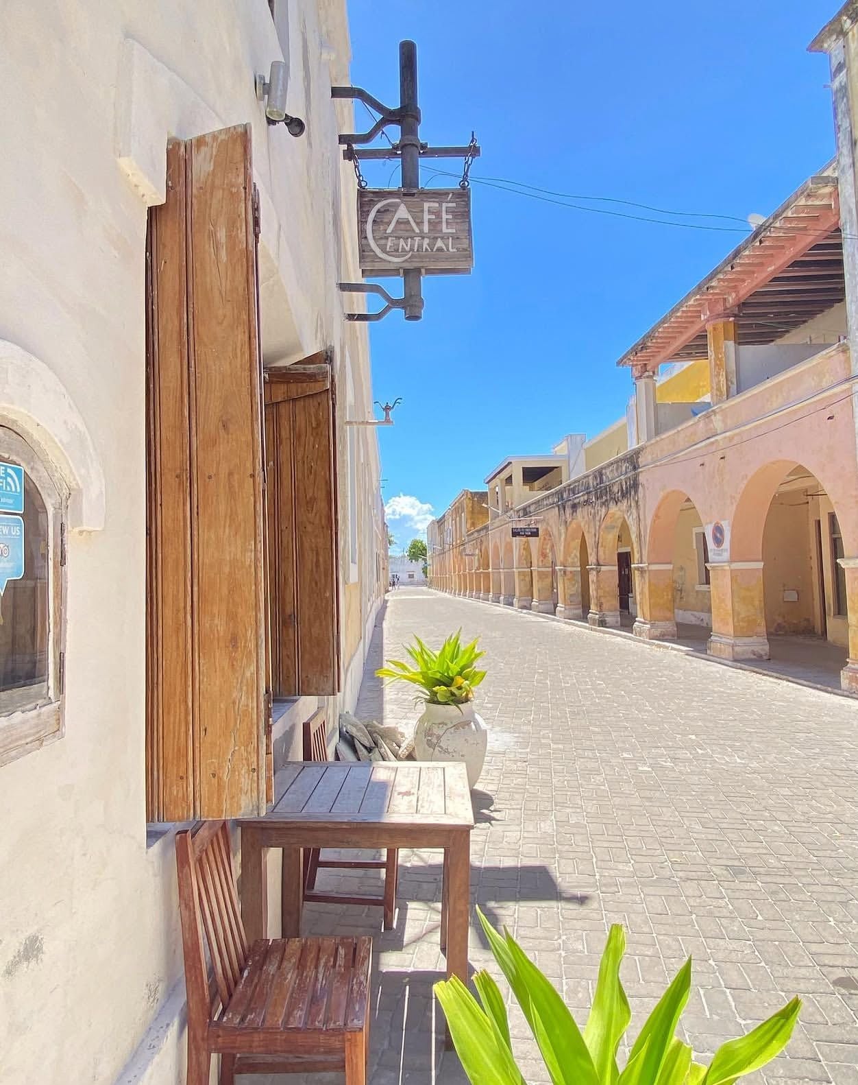 Un café con mesas y sillas de madera frente a un edificio en una calle empedrada.