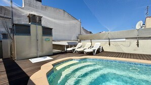Piscina no terraço com água azul cristalina, cadeiras de espreguiçadeira brancas e uma barreira de segurança com rede.