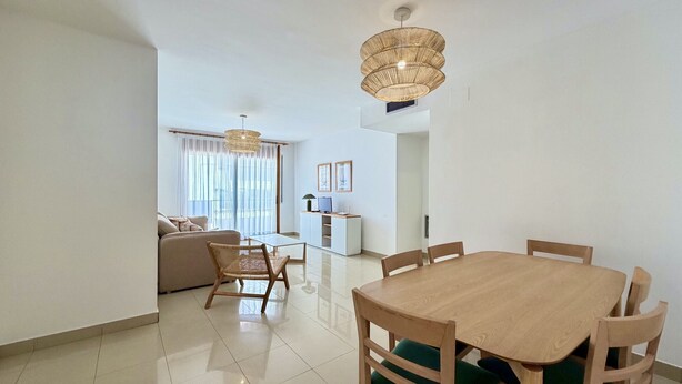 Uma sala de estar moderna com área de jantar, um sofá, uma mesa e um lustre.