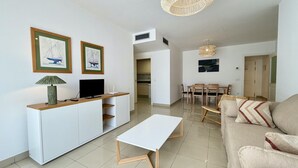 Uma sala de estar moderna com um sofá branco, uma mesa de centro, uma televisão e quadros nas paredes.