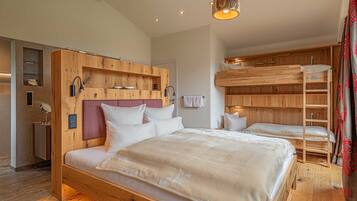 A bedroom with a large bed, a wooden headboard, a built-in shelf, a bedside table, and a bunk bed.
