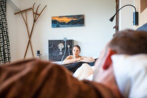 A room with a bed, a painting, a headboard, and a wall-mounted lamp.