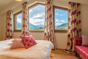 A bedroom with a bed, two windows, a sofa, and curtains with heart patterns.