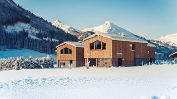 A wooden cabin with a stone facade, set against a snowy mountain backdrop.