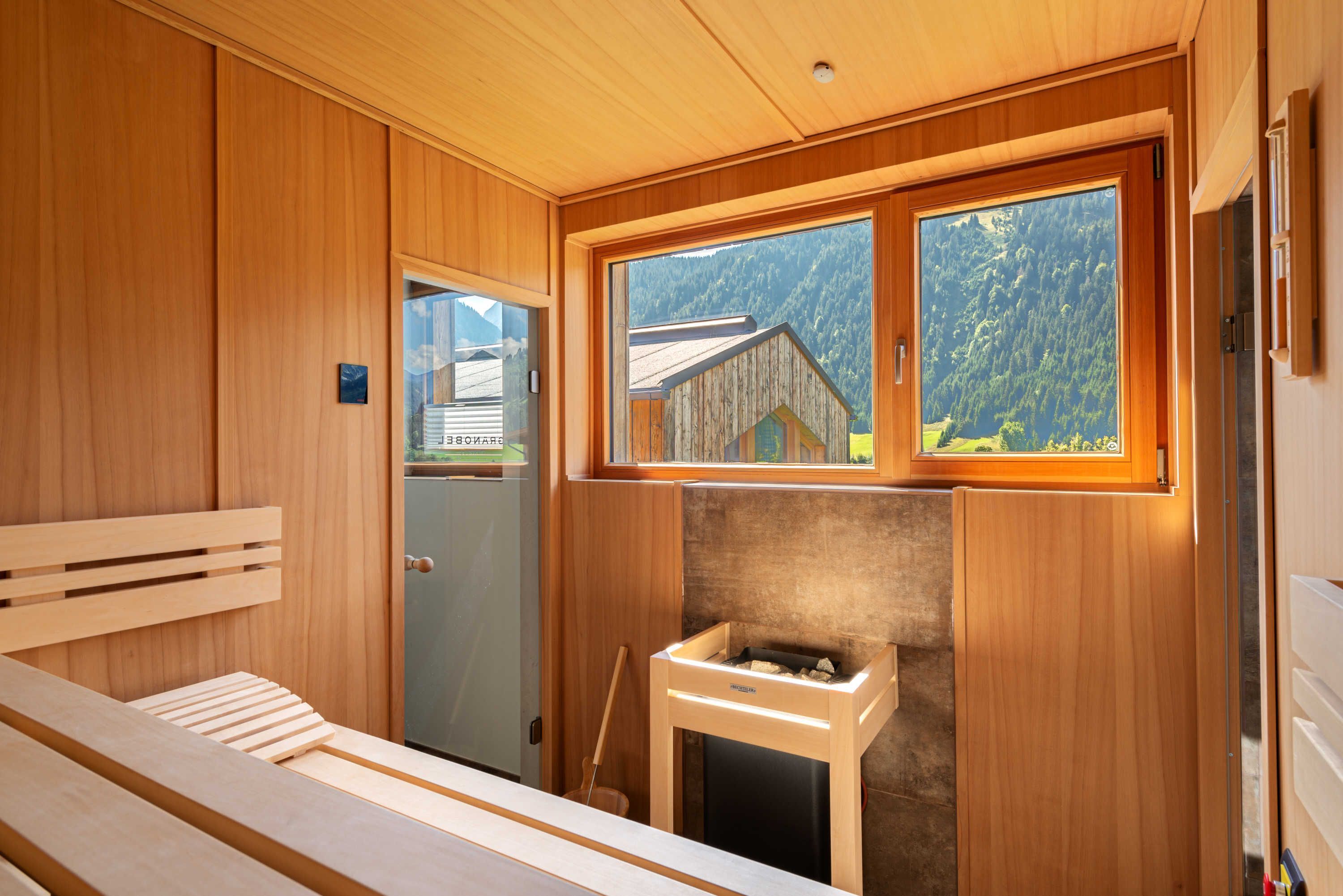 A wooden cabin interior with a bench, a fireplace, and a window overlooking a mountain.