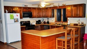 A kitchen with wooden cabinets, a refrigerator, a microwave, a coffee maker, and a blender. - Beach House Rental Duck, NC (Duck)