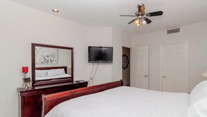 Un dormitorio con cama, cómoda, televisor, ventilador de techo y puerta.