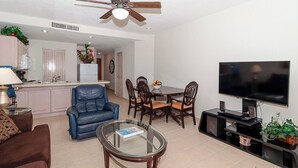 Una sala de estar con un sofá, una mesa de centro de vidrio, un televisor y un comedor con sillas y una mesa.