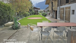 A patio area with a table and chairs, a small lawn, and a view of mountains.