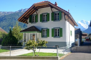 A two-story house with green shutters, a white facade, and a sloped roof. - Jungfrau Family Holiday Home, 5 bedrooms, sleeps 10, garden, BBQ, and parking (Matten bei Interlaken)