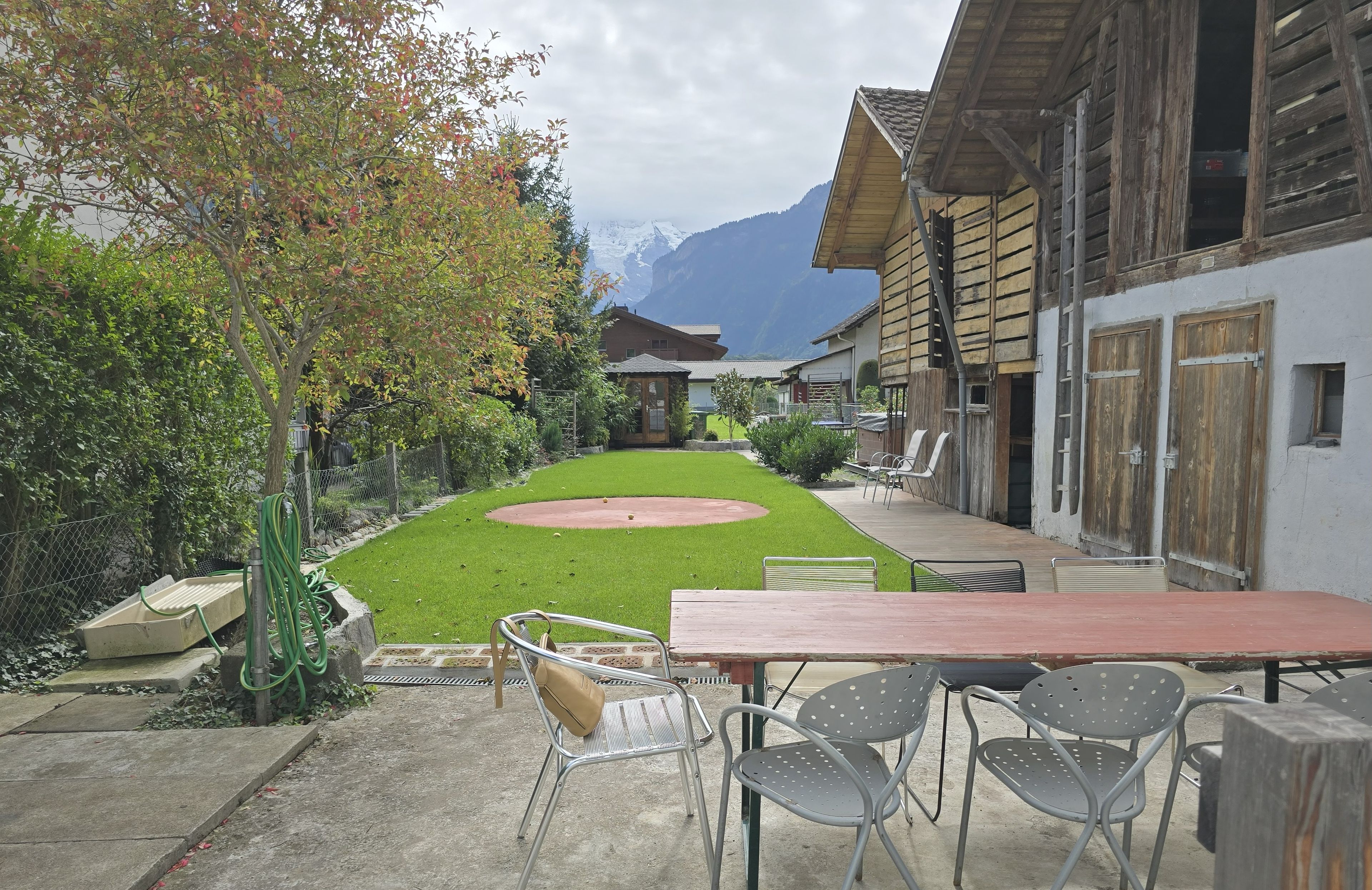 Un patio con mesa y sillas, un pequeño jardín y vistas a montañas.