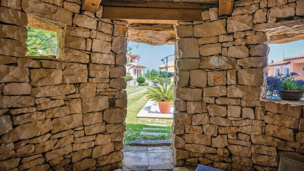 A stone archway leading to a courtyard with a potted plant and a view of a house. - Amazing home in Labin (Labin)