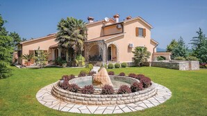 A two-story house with a stone fountain in the front garden, surrounded by well-maintained grass and shrubs. - Amazing home in Labin (Labin)