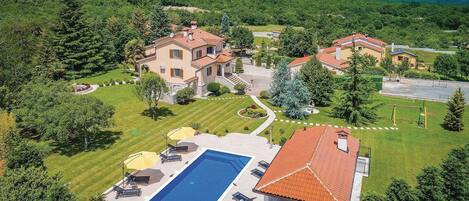 A large house with a swimming pool, surrounded by lush greenery and a view of the sea.