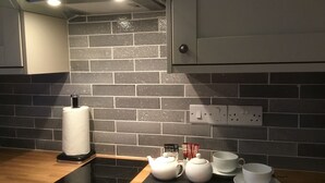 Una cocina con una placa de inducción negra, un hervidor blanco, una taza blanca y un platillo blanco sobre una encimera de madera.