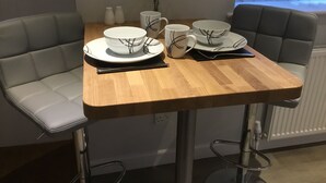 Una mesa de comedor con un juego de platos y tazones blancos con diseños negros, acompañado de tazas a juego y un florero con flores amarillas.