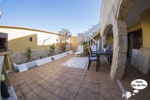 Un patio con un muro de piedra, un banco blanco y una mesa con sillas.
