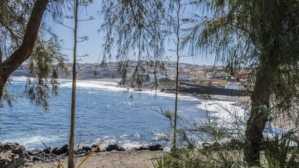 Vista costera con playa arenosa, costa rocosa y un pueblo lejano.
