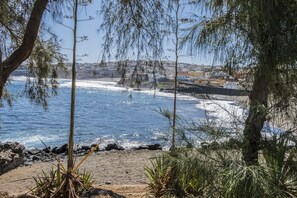 A coastal view with a sandy beach, rocky shoreline, and a distant town.