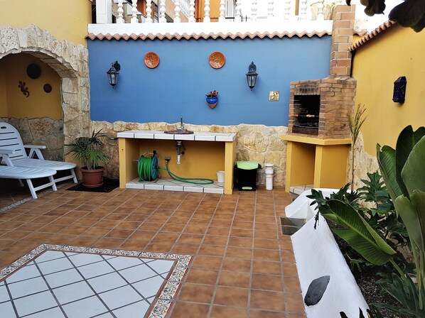Un patio con suelo de baldosas, pared de piedra, pared azul con placas decorativas, horno de ladrillo y una pequeña zona de fregadero.