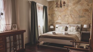 Un dormitorio con pared de piedra, una cama con dos almohadas, una mesita de noche y una silla.