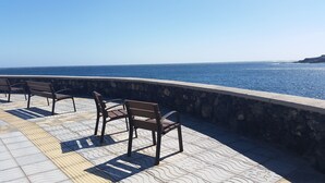 Un paseo marítimo junto a la playa con muros de piedra y bancos con vistas al océano.