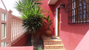 Un edificio rojo con una cerca blanca, una planta en maceta y una puerta con reja de metal.