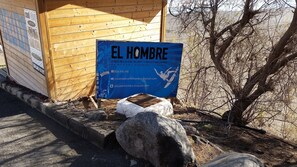 Una estructura de madera con un letrero que anuncia una tienda de alquiler de tablas de surf llamada 'El Hombre'.