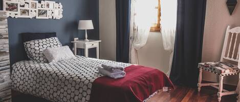 A neatly arranged bedroom with a bed, a bedside table with a lamp, a chair, and a window with curtains.