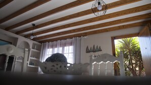Una habitación con vigas de madera en el techo, una silla blanca, una mesa y una ventana con cortinas.