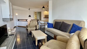 A living room with a sofa, armchairs, a coffee table, a TV, and a dining area with chairs and a table.