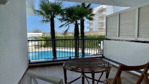 A balcony with a pool, palm trees, and a view of other buildings.